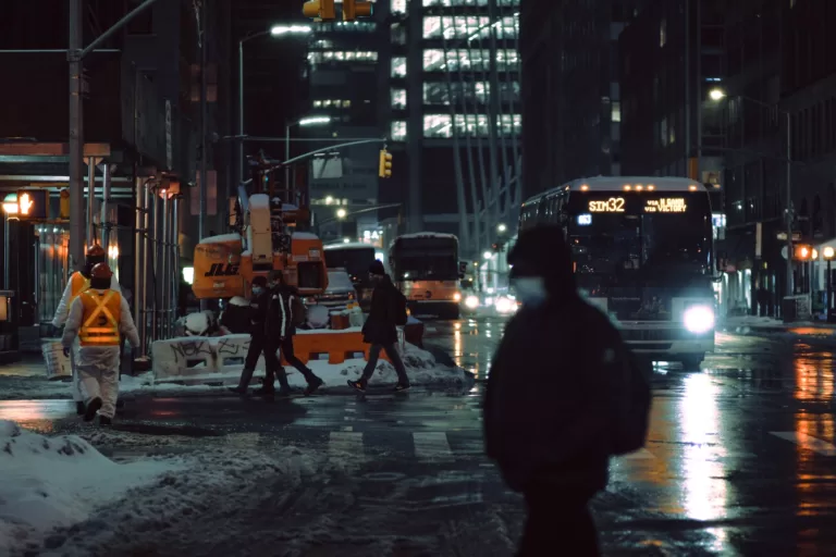 people walking on snowy road with bus on dark street